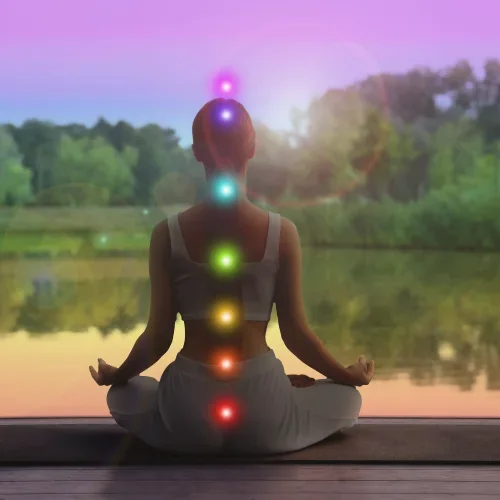 Persona in meditazione con i centri energetici illuminati, al tramonto sul lago