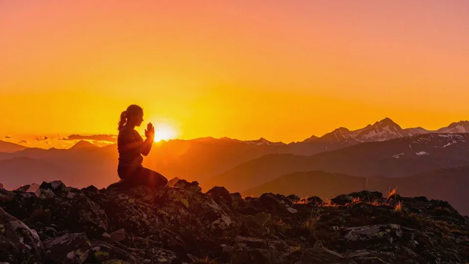Silhouette di una persona in raccoglimento davanti al sole che sorge sulle montagne