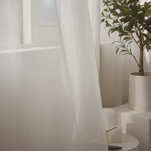 Angolo di una stanza luminosa con tenda bianca e pianta verde